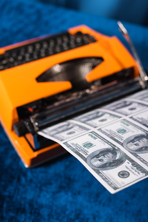 high angle view of blurred vintage typewriter and dollar banknotes on blue table