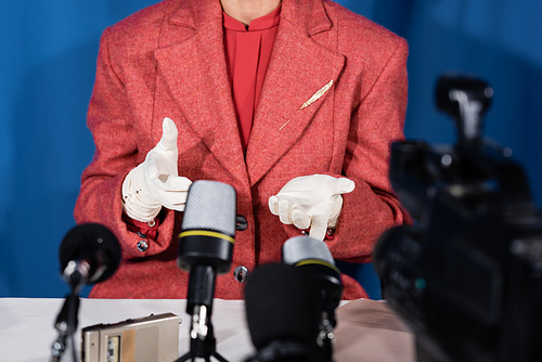 cropped view of woman in red blazer and white gloves pointing with fingers on blue background