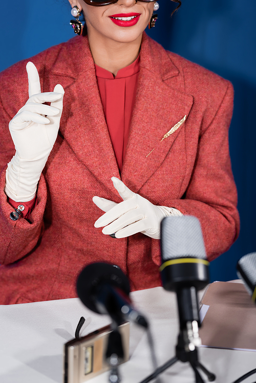 partial view of vintage style woman pointing with fingers near microphones during interview of blue background
