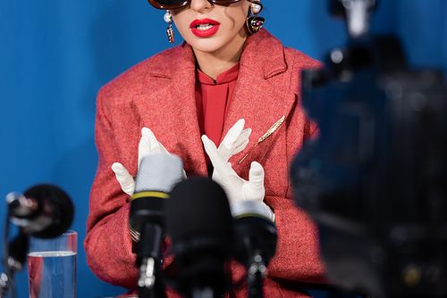 blurred microphones near cropped woman in white gloves giving interview on blue background
