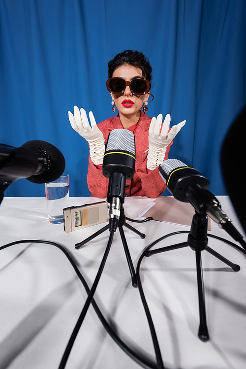 vintage style woman in white gloves near dictaphone and microphones on blue background