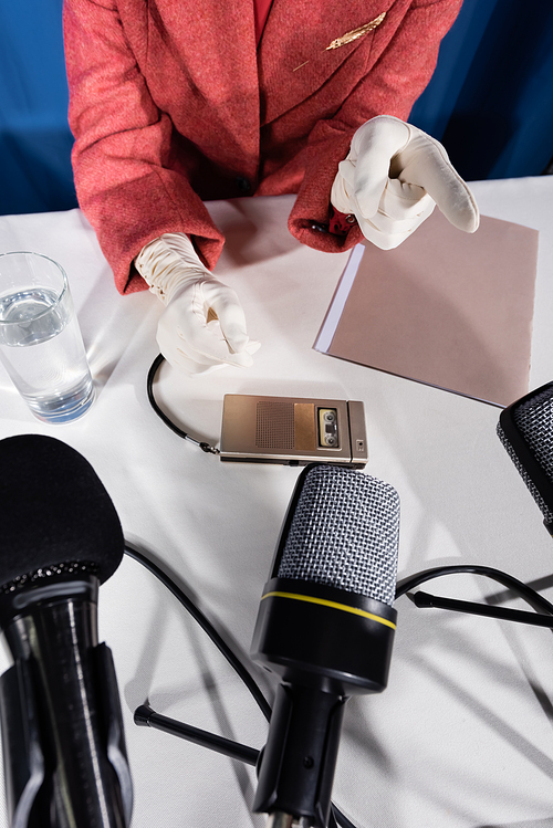 top view of cropped woman in white gloves pointing with finger near microphone and dictaphone