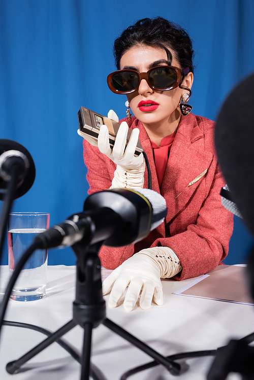 blurred microphones near retro style woman holding dictaphone during interview on blue background