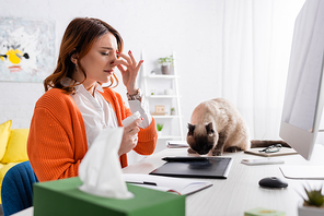allergic woman sneezing near cat sitting on work desk near graphic tablet