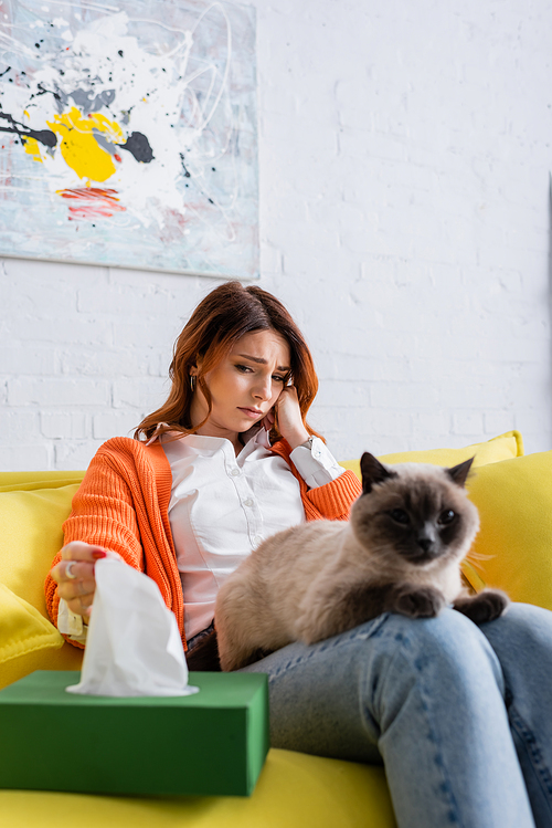 upset allergic woman taking paper napkin from pack near blurred cat