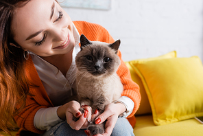 young woman smiling while sitting with cat on sofa at home