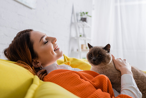 side view of happy woman with closed eyes relaxing with cat on couch