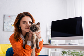 cheerful woman  while embracing cat near monitor with blank screen
