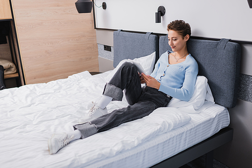 Young woman using digital tablet on bed in hotel room