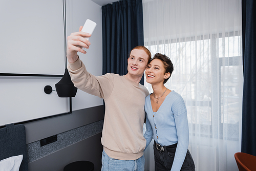 Smiling couple taking selfie on smartphone in modern hotel room