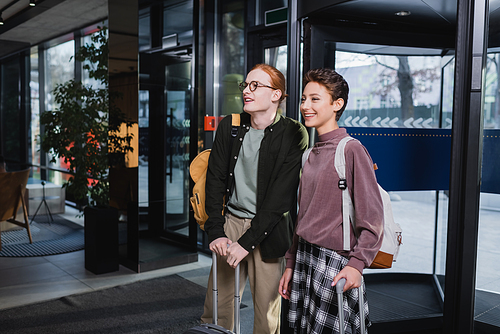 Positive couple with suitcases and backpacks standing in hotel lobby