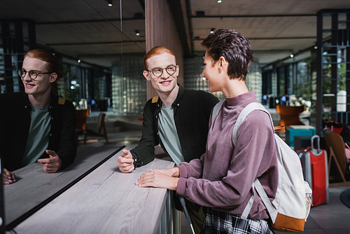 Cheerful couple with backpack and suitcase standing near hotel reception