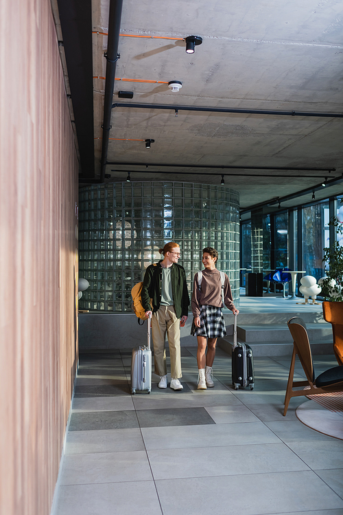 Smiling couple with baggage walking in hotel lobby