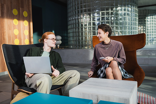 Smiling couple using smartphone and laptop in lobby of hotel