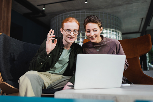 Young smiling tourists having video call on blurred laptop in hotel lobby