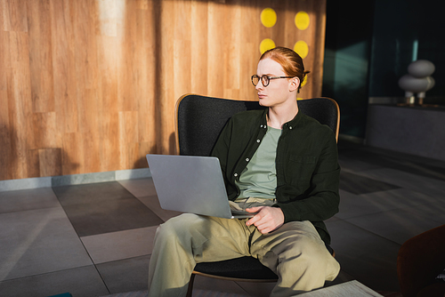 Young redhead freelancer using laptop in hotel lobby