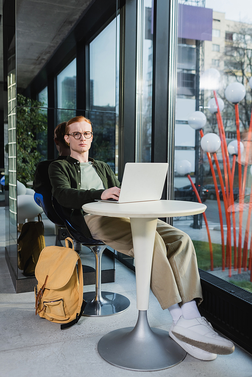 Red haired man using laptop near backpack and  in hotel lobby