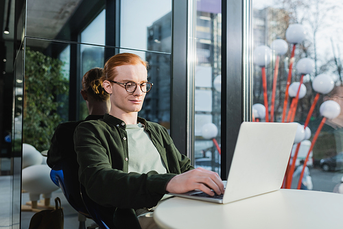 Red haired man in eyeglasses using laptop in hotel lobby