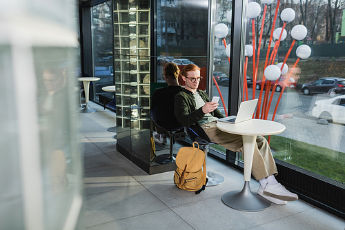 Young freelancer using devices near backpack in hotel lobby