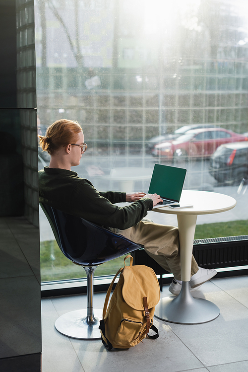 Redhead freelancer using laptop with chroma key near backpack in hotel lobby