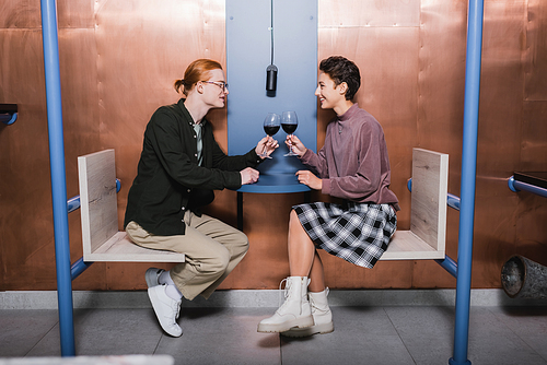 Side view of positive couple holding wine in cafe of hotel