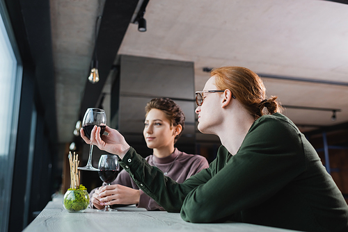 Young man holding wine near blurred girlfriend in hotel