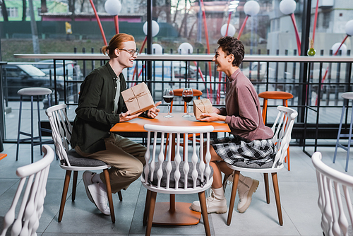 Young couple holding gifts near glasses of wine in hotel cafe