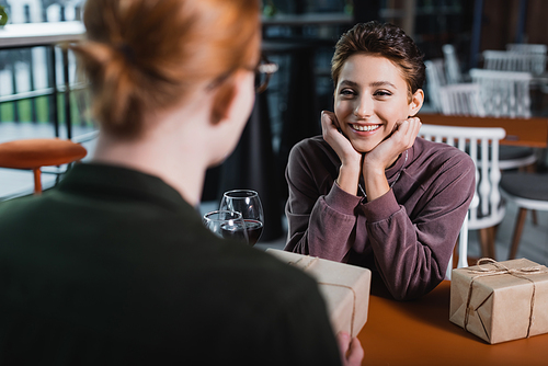 Joyful woman looking at blurred boyfriend with present near wine in hotel cafe