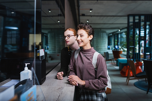 Positive woman with backpack standing near boyfriend on hotel reception