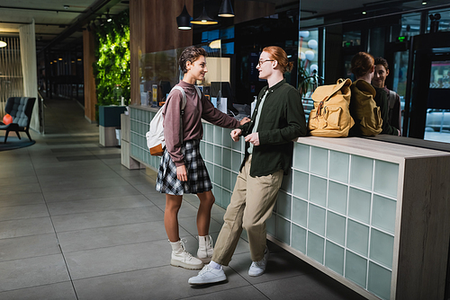 Side view of smiling tourists with backpacks talking near reception in hotel