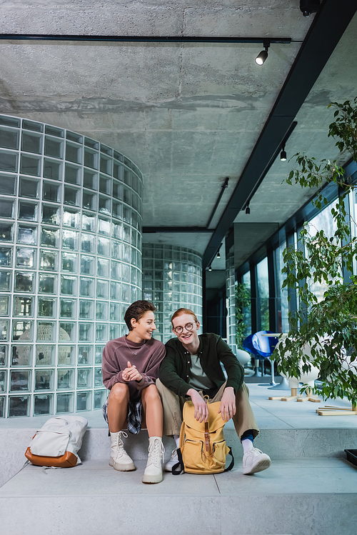 Smiling woman talking to boyfriend near backpacks on stairs in hotel