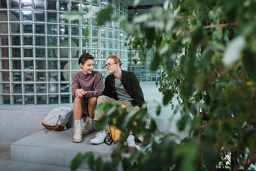 Positive couple of tourists sitting near backpacks and plants in hotel