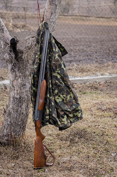 camouflage jacket hanging on tree near rifle in woods
