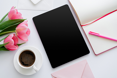 top view of cup of coffee near pink tulips and digital tablet with blank screen and notebook on white