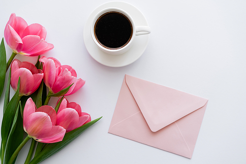 top view of bouquet of tulips near cup of coffee and pink envelope on white
