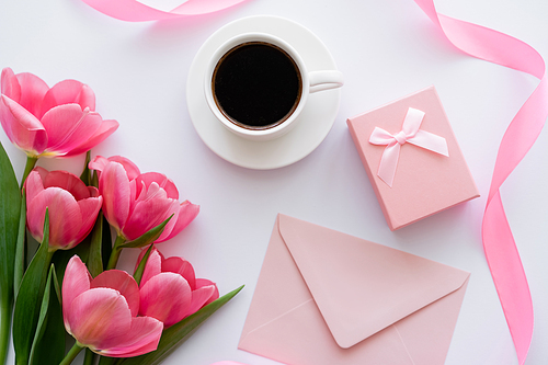 top view of bouquet of tulips near cup of coffee, gift box and pink envelope on white