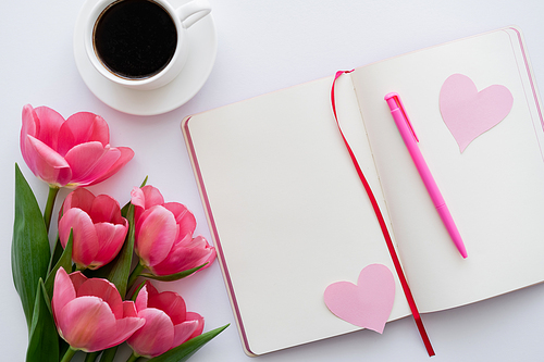 top view of tulips near notebook with paper hearts and cup of coffee on white