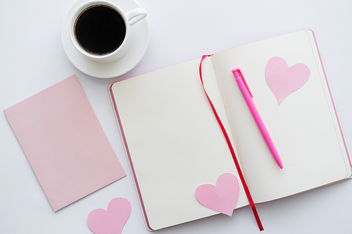 top view of notebook with paper hearts and cup of coffee near envelope on white