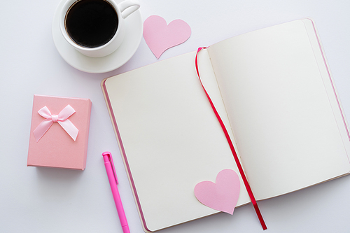top view of notebook with paper hearts and cup of coffee near envelope on white