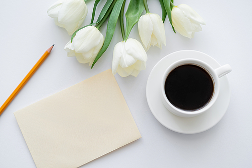 top view of envelope with pencil near cup with coffee and tulips on white