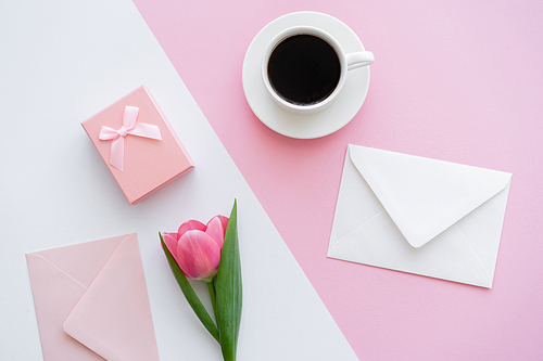 top view of envelopes near cup with coffee, gift box and tulip on white and pink