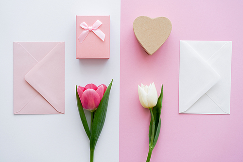 top view of envelopes near gift boxes and tulips on white and pink