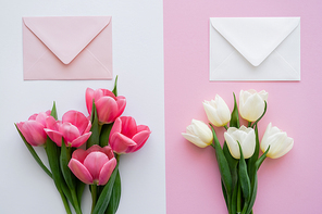 top view of blossoming tulips near envelopes on white and pink