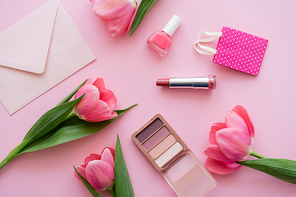 top view of blooming tulips near decorative cosmetics and envelope on pink