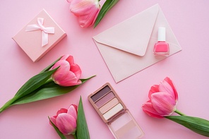 top view of blooming tulips near decorative cosmetics, present and envelope on pink