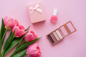 top view of blooming tulips near decorative cosmetics and gift box on pink