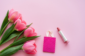 top view of blooming tulips near lipstick and small shopping bag on pink