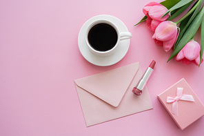 top view of blooming tulips near lipstick, envelope and cup of coffee on pink