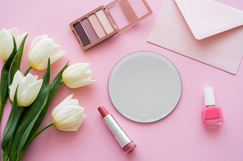 top view of white tulips near envelope and decorative cosmetics on pink