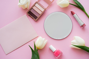 top view of white tulips near mirror, envelope and decorative cosmetics on pink
